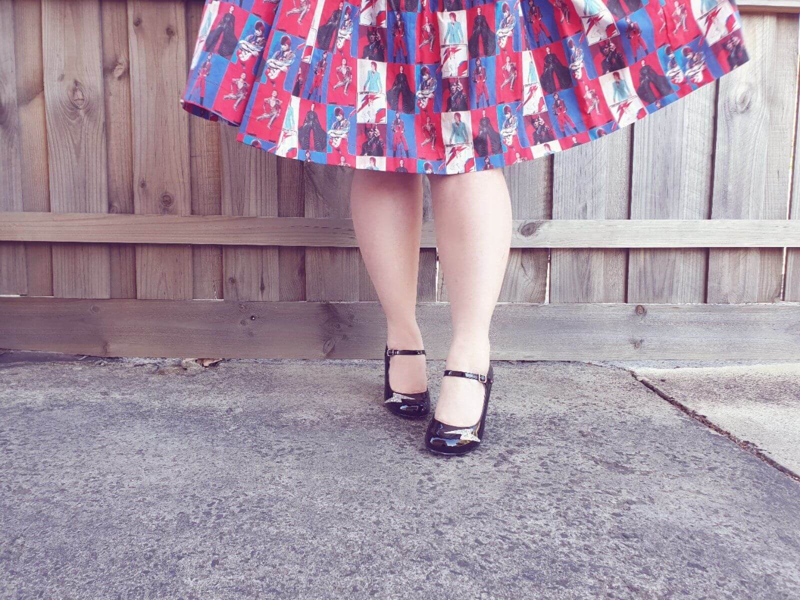 Close-up of stylish legs in a patterned skirt and shiny black shoes, showcasing a playful, vintage-inspired look.