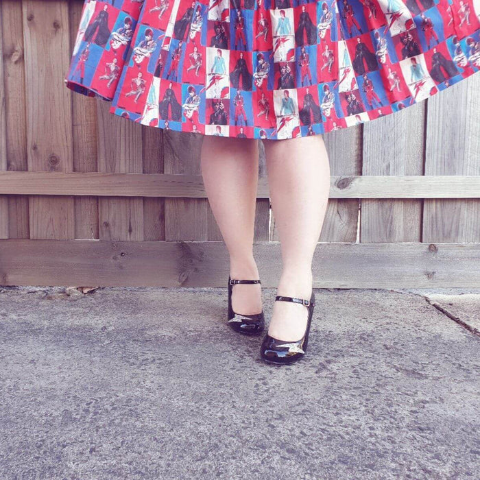 Close-up of stylish legs in a patterned skirt and shiny black shoes, showcasing a playful, vintage-inspired look.